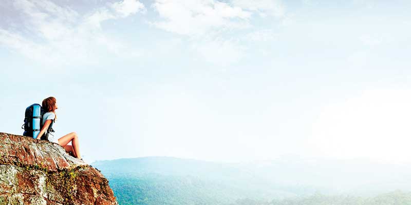 A Solo Woman Traveller Sitting and Starring From the Top Of the Mountain.