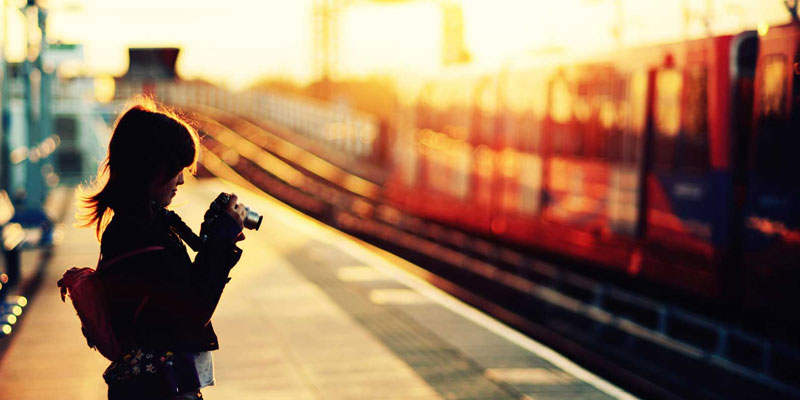 A Woman Traveller Standing In The Railway Station With Camera